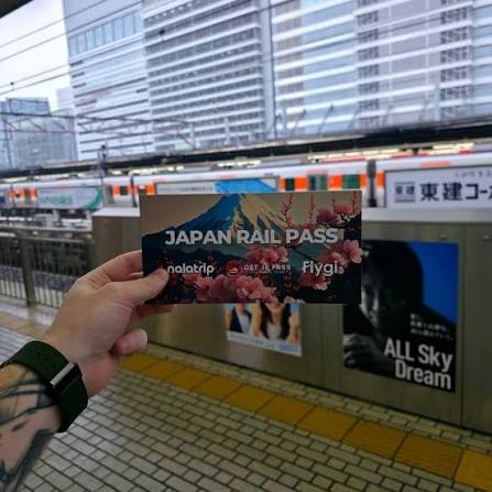 Japan Rail Pass voucher folder held up on a Tokyo station platform