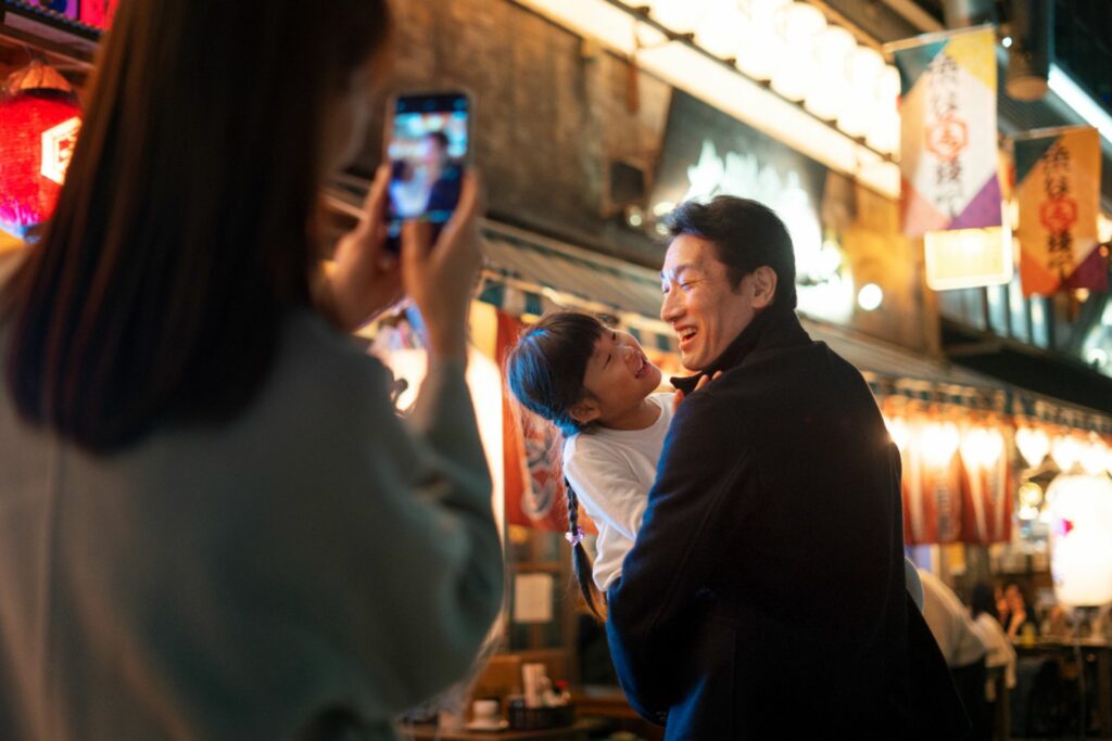 Family enjoying an evening street in Japan while taking photos with a phone