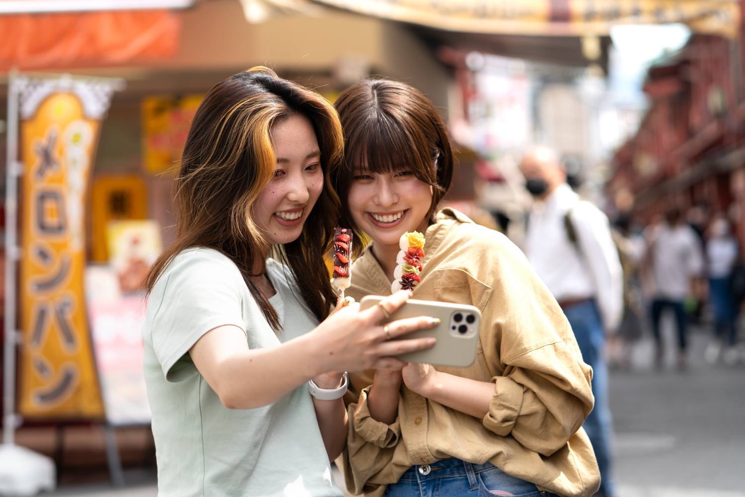 Two friends checking a smartphone on a busy street in Japan